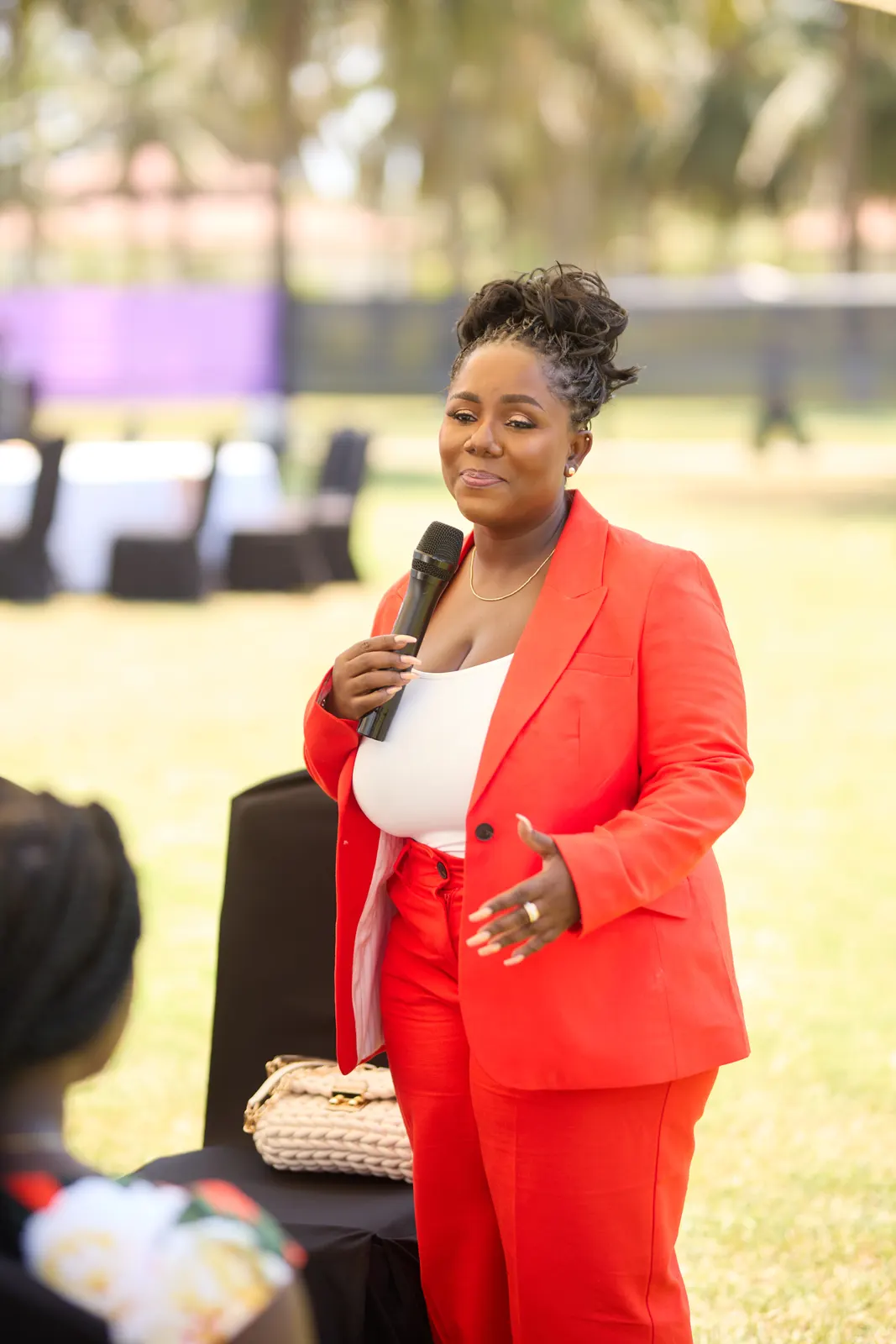 Host in a bright red trouser suit speaking into a microphone outdoors