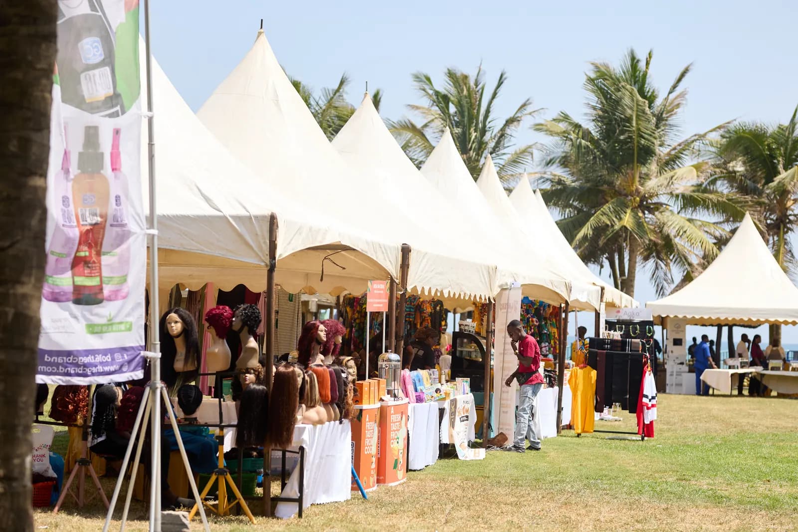 Row of white peaked vendor tents beside palm trees on a sunny lawn