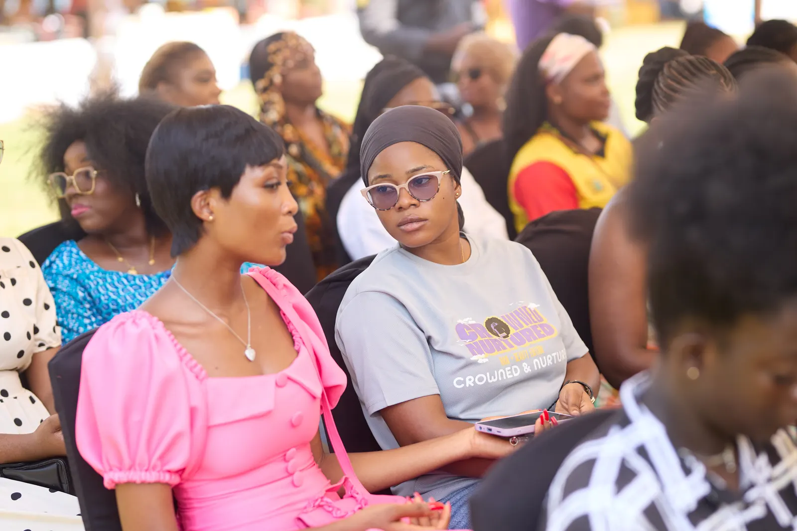 Guests in the audience, one in a pink dress, listening intently