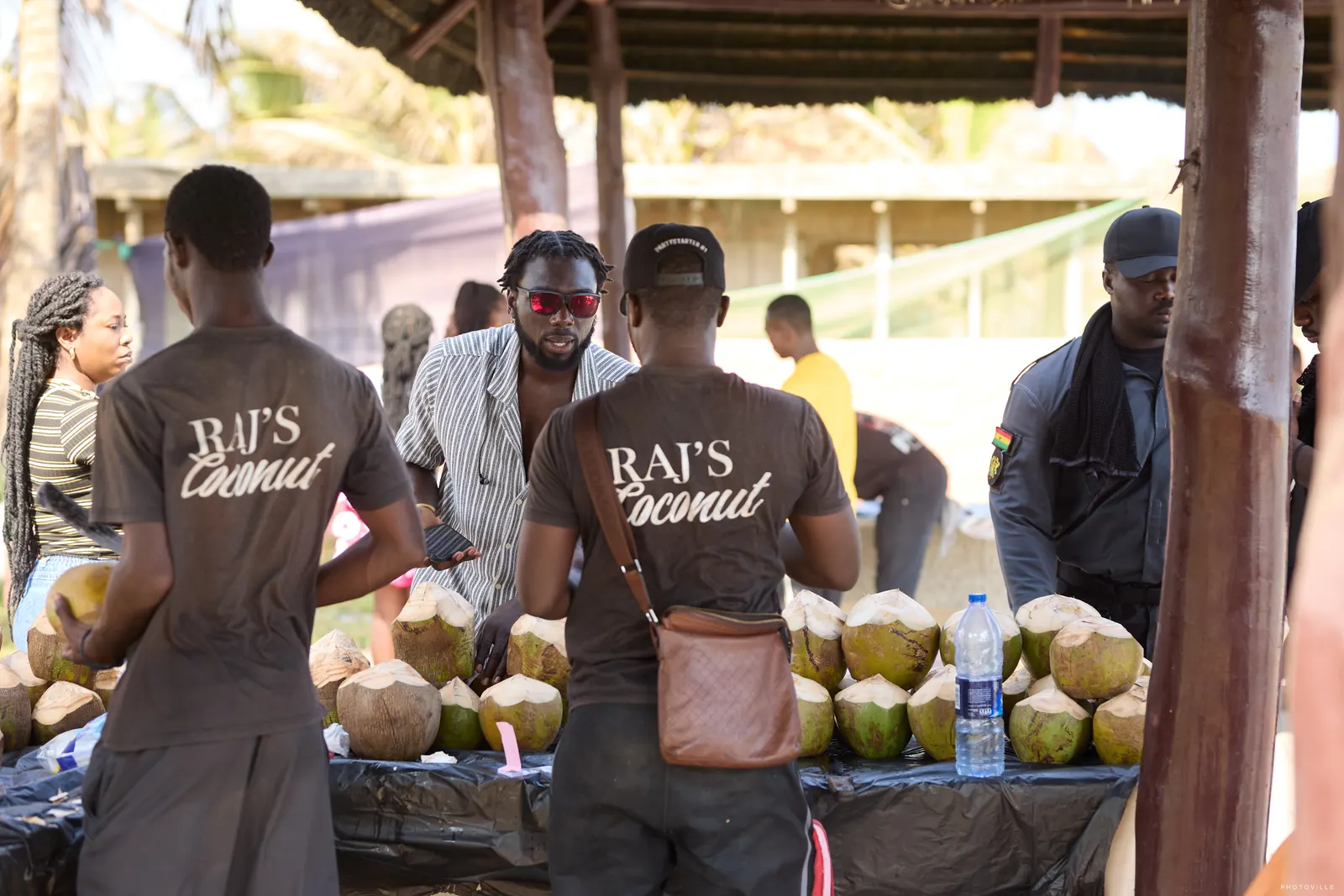 Vendors in branded T-shirts serving fresh coconuts at a stall