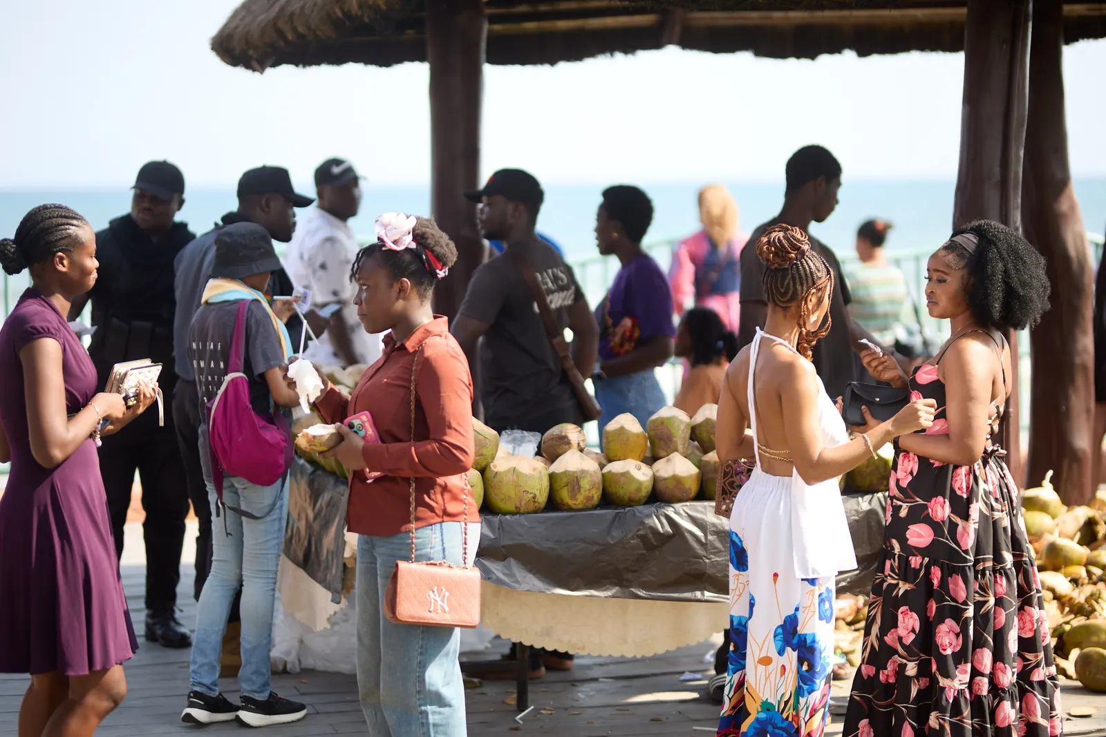 Guests gathered at a fresh coconut stand under a thatched shelter by the sea