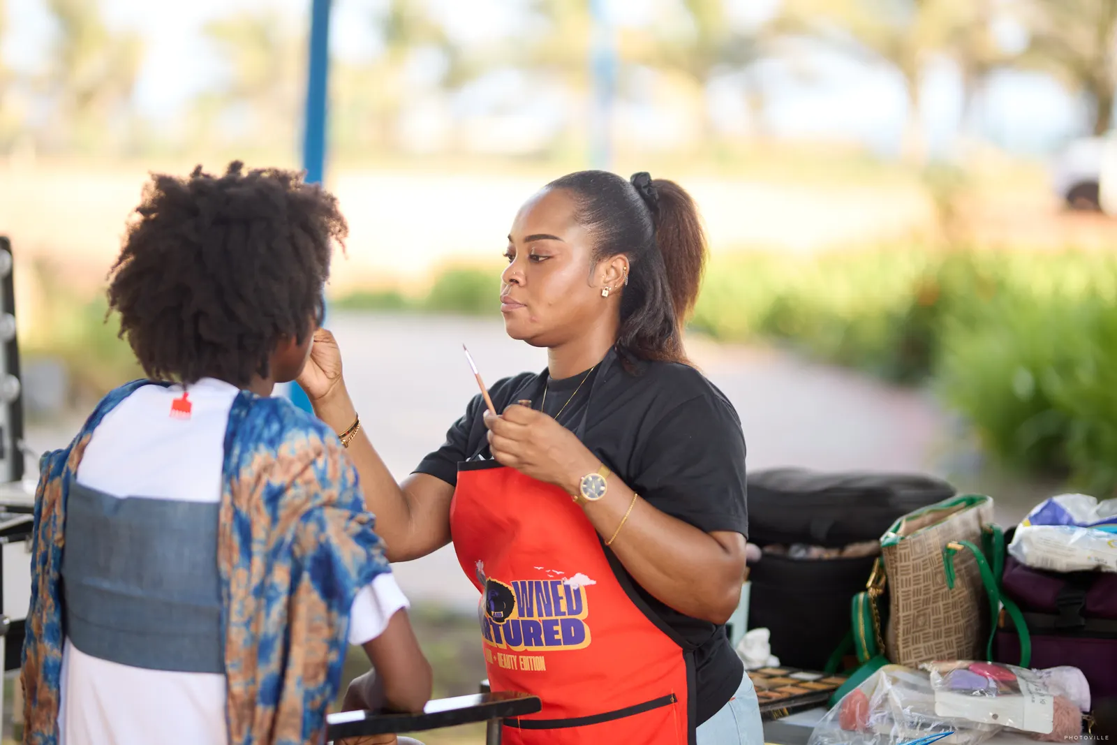 Stylist in a red apron working on a client's hair at an outdoor station