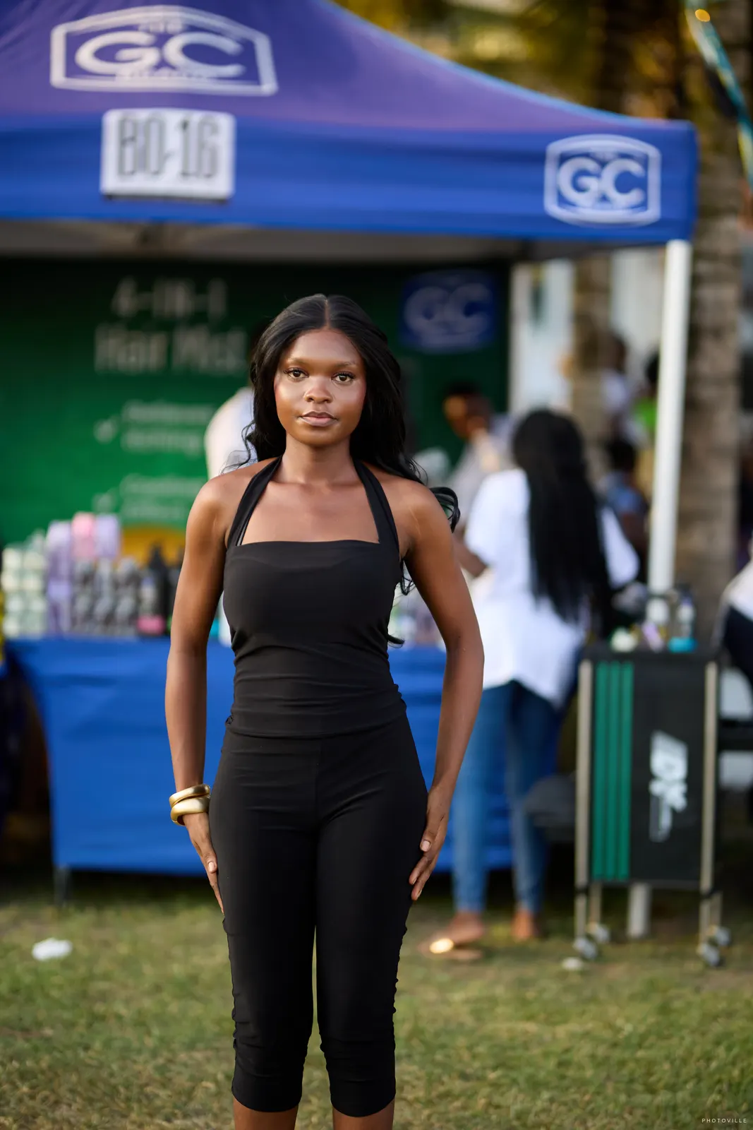 Woman in a black jumpsuit standing in front of a hair-care brand tent