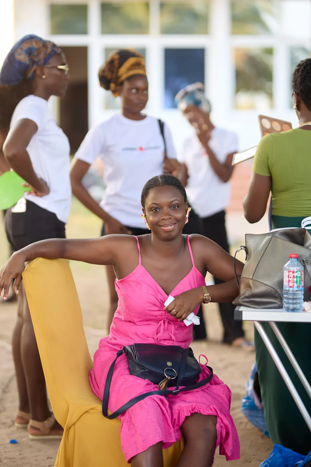 Smiling woman in a pink dress seated at an outdoor beauty station
