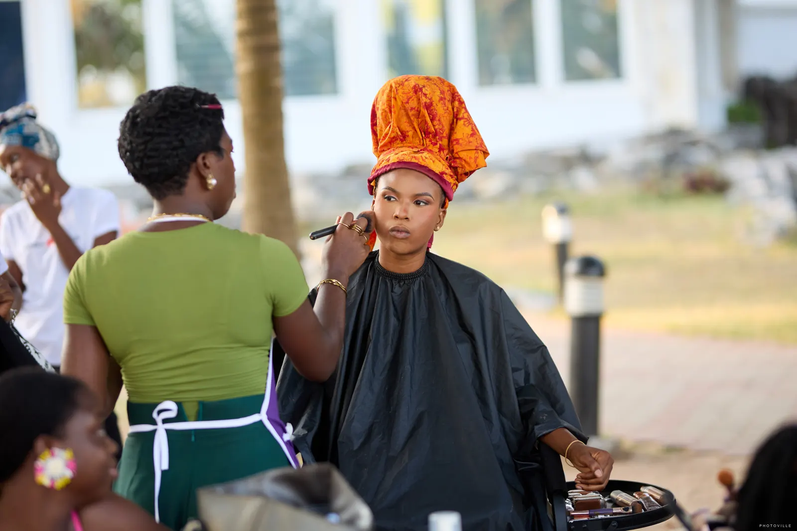 Makeup artist applying makeup to a client wearing an orange headwrap