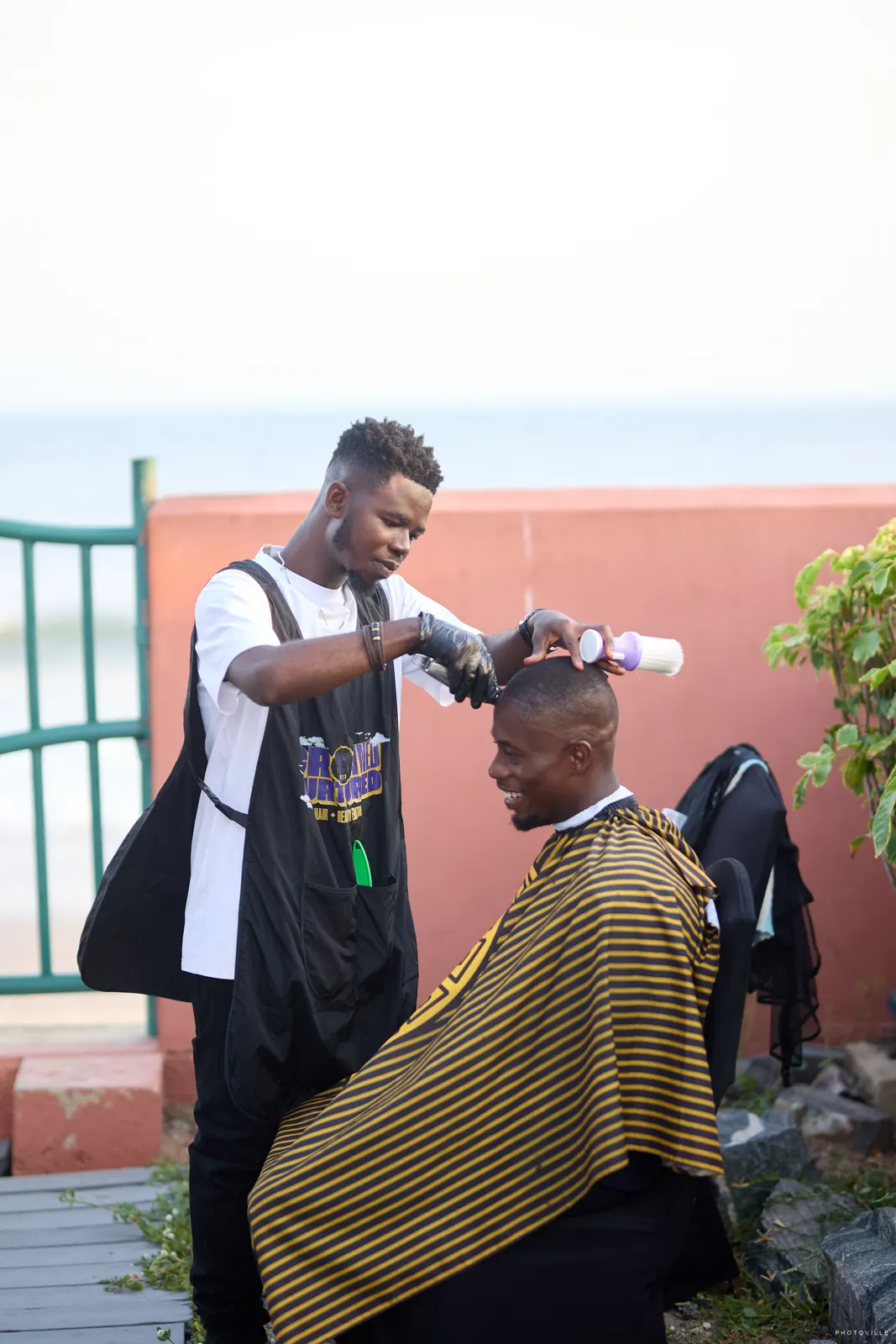 Barber giving a haircut beside a seaside railing