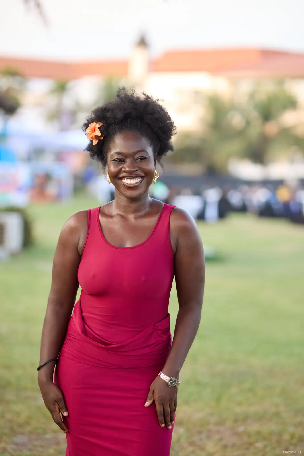 Woman in a red dress with a flower in her hair smiling on the lawn at golden hour