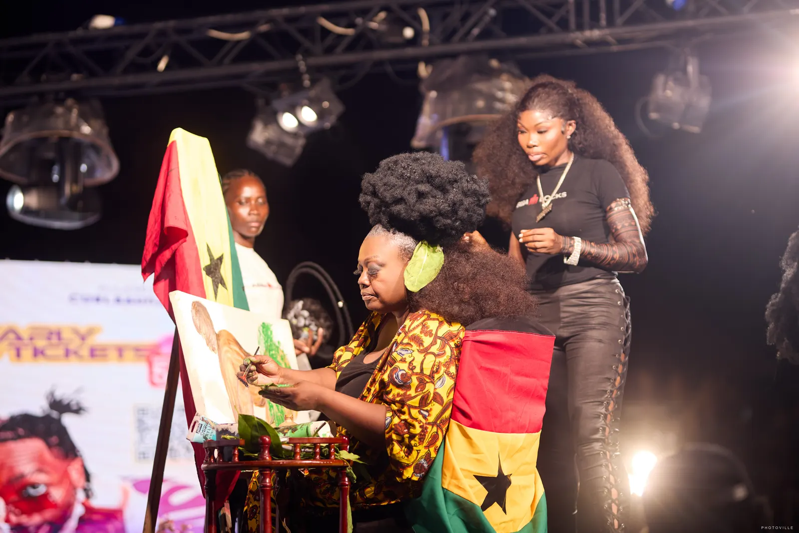 Live painting on stage beside a Ghana flag under stage lights