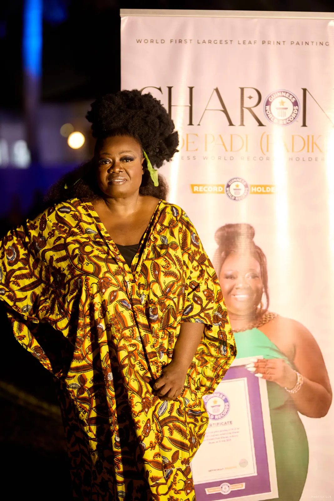 Woman in a gold and black print kaftan beside a pull-up banner at night