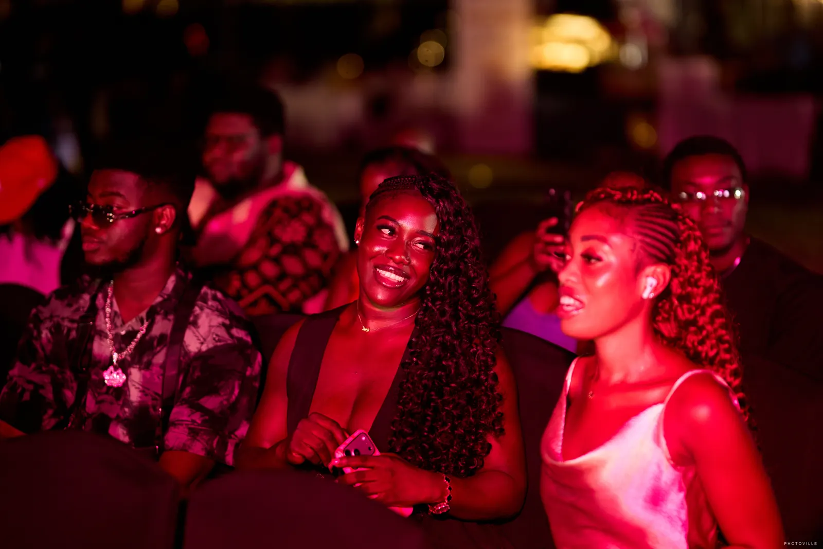 Guests smiling in the audience under red and purple stage lights