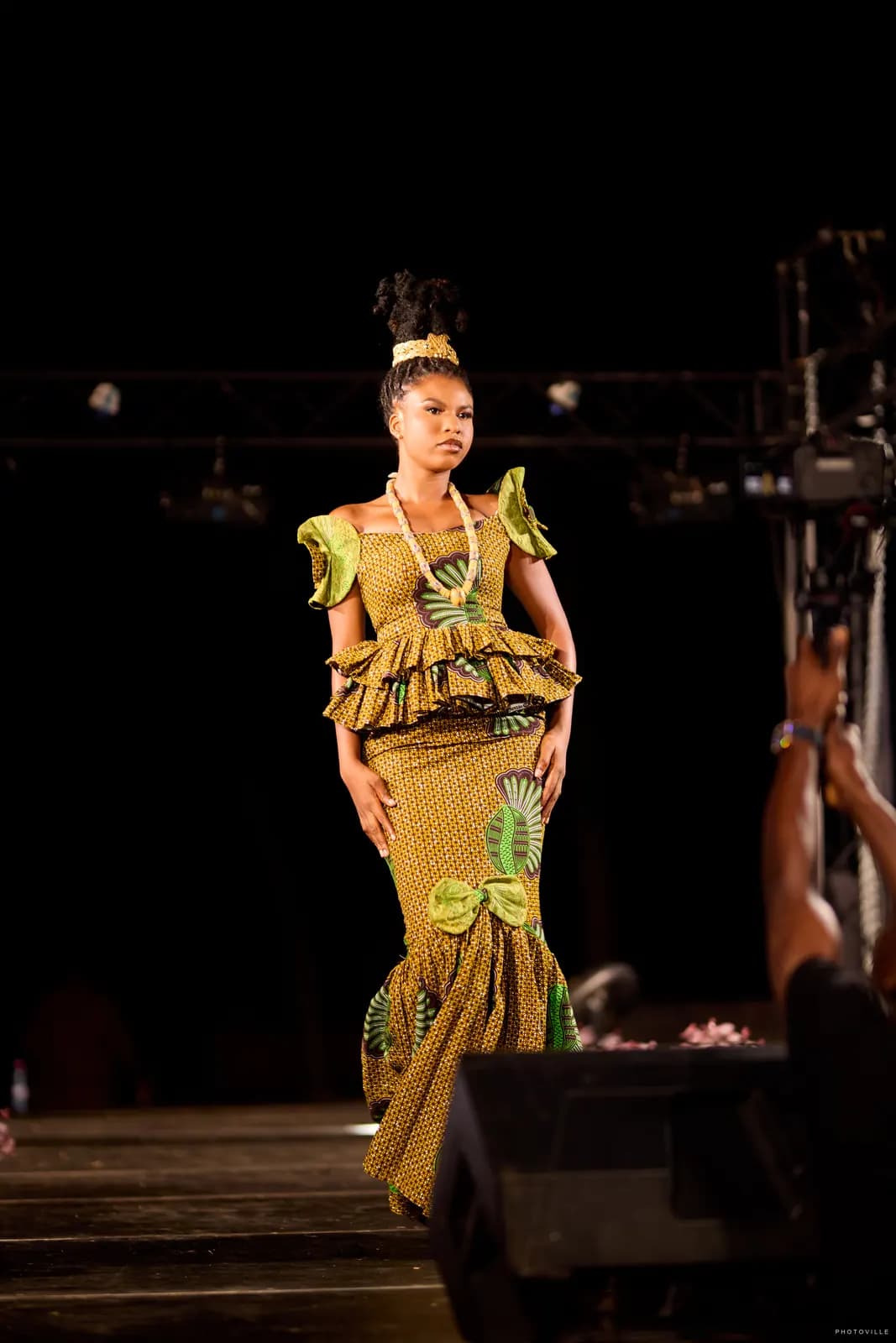 Model in an olive print peplum mermaid gown walking the night runway