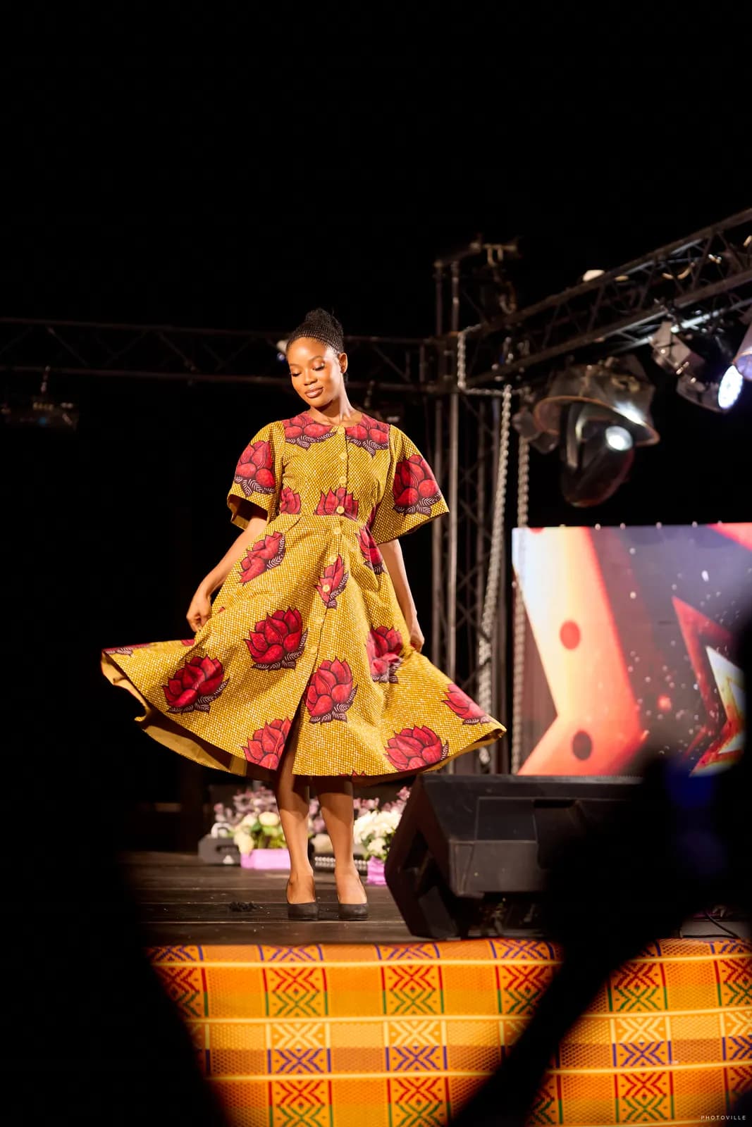 Model twirling in a red-floral print dress on a kente-draped runway